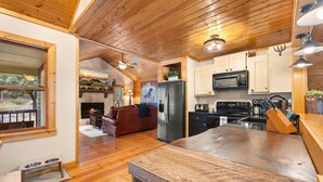 A cozy cabin interior with a wooden ceiling, a kitchen with modern appliances, a fireplace, and a dining area. - Creekfront: Views, Hot Tub, Fire Pit & Game Room (Blue Ridge)