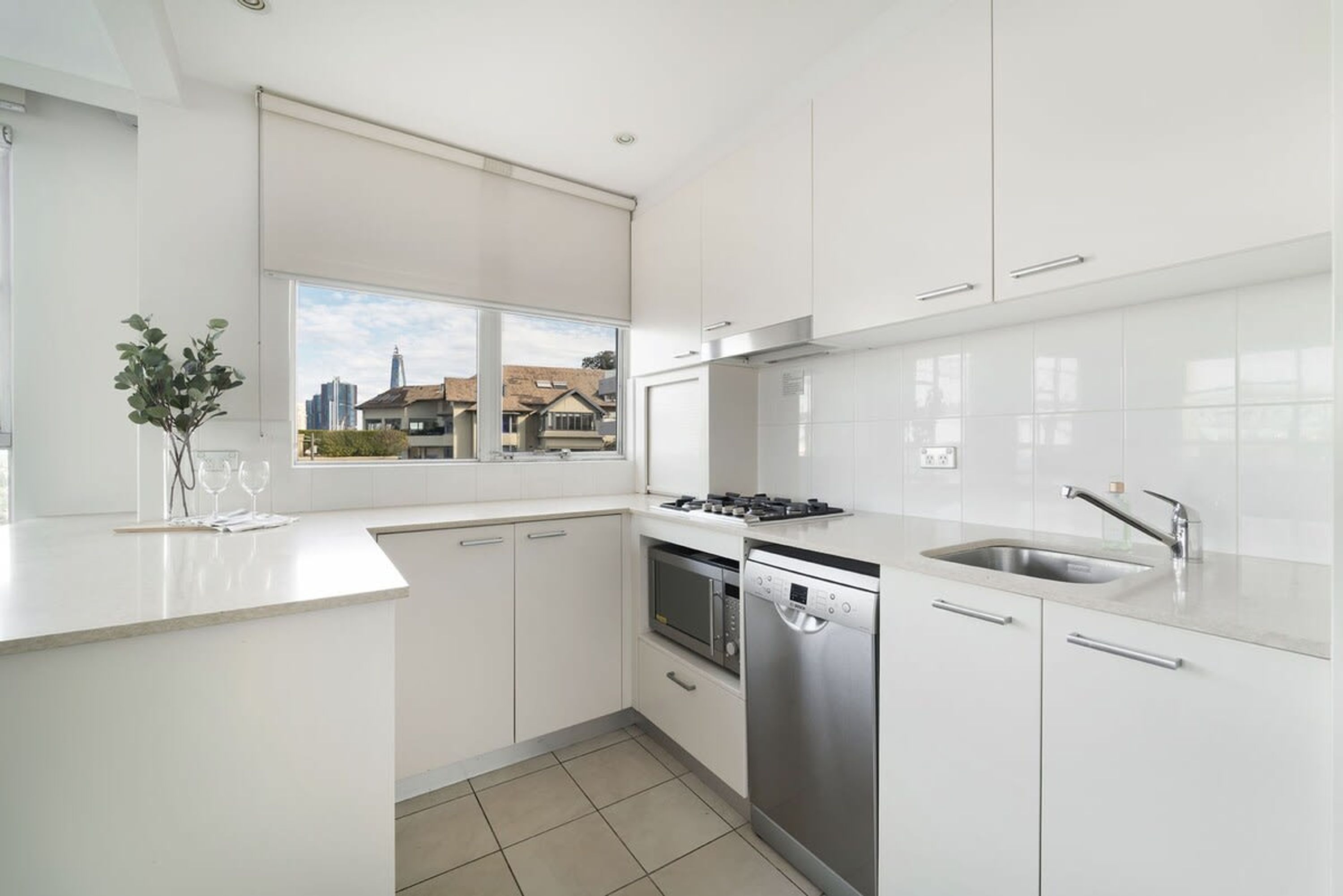 Una cocina moderna con armarios blancos, estufa a gas, lavavajillas y ventana con vista a una zona residencial.