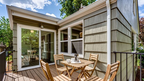 A wooden deck with a table and chairs, a sliding glass door, and a small outdoor kitchen area. - Stunning U of O Home – Just Steps from Hayward Field! (Eugene)