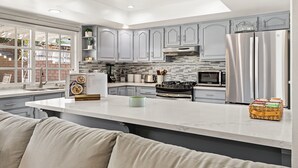 A modern kitchen with grey cabinets, a stainless steel refrigerator, and a large island with a green mug.