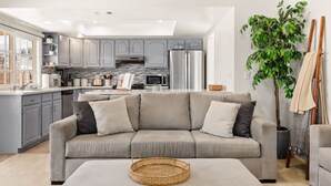 A modern kitchen with grey cabinets, a stainless steel refrigerator, and a large window.