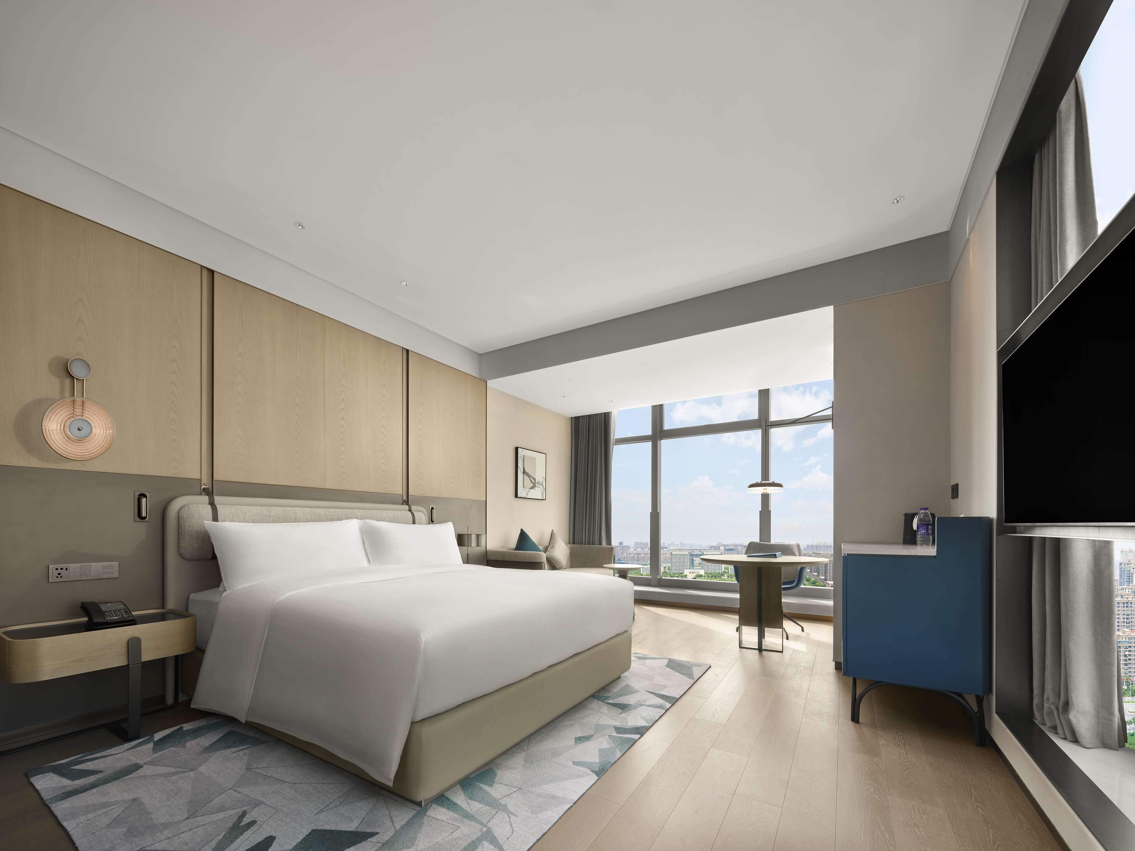A modern hotel room with a large bed, a desk, and a view of the city.
