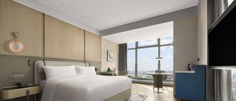 A modern hotel room with a large bed, a desk, and a view of the city.
