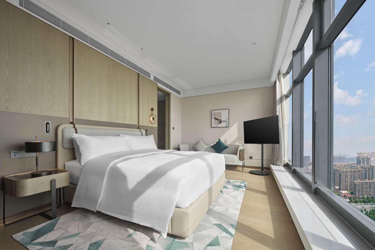 Una habitación de hotel moderna con una cama grande, televisión y vista a la ciudad.