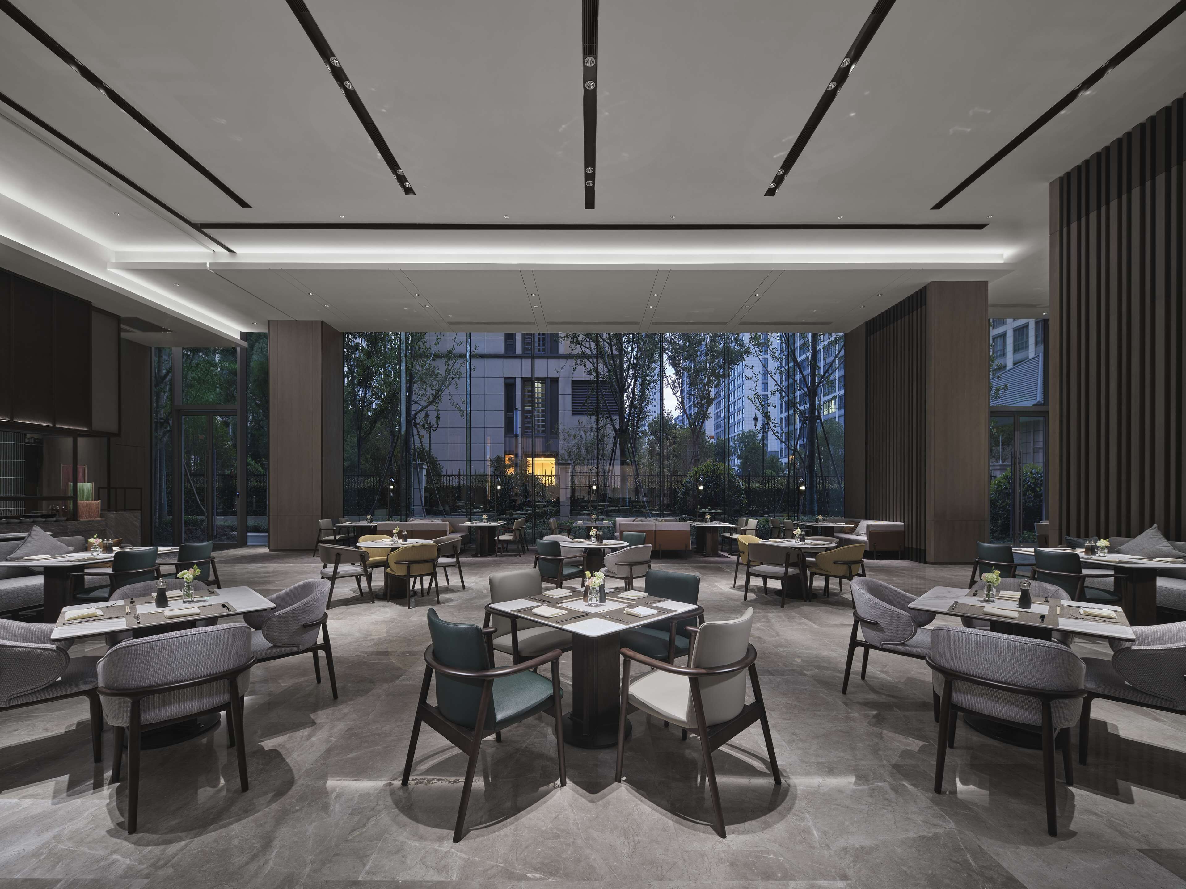 Um restaurante moderno com várias mesas e cadeiras, grandes janelas com vista para a cidade e um design de interiores contemporâneo.