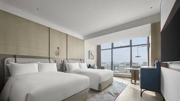 Habitación de hotel moderna con dos camas, un escritorio y un ventanal amplio que ofrece vistas a la ciudad.