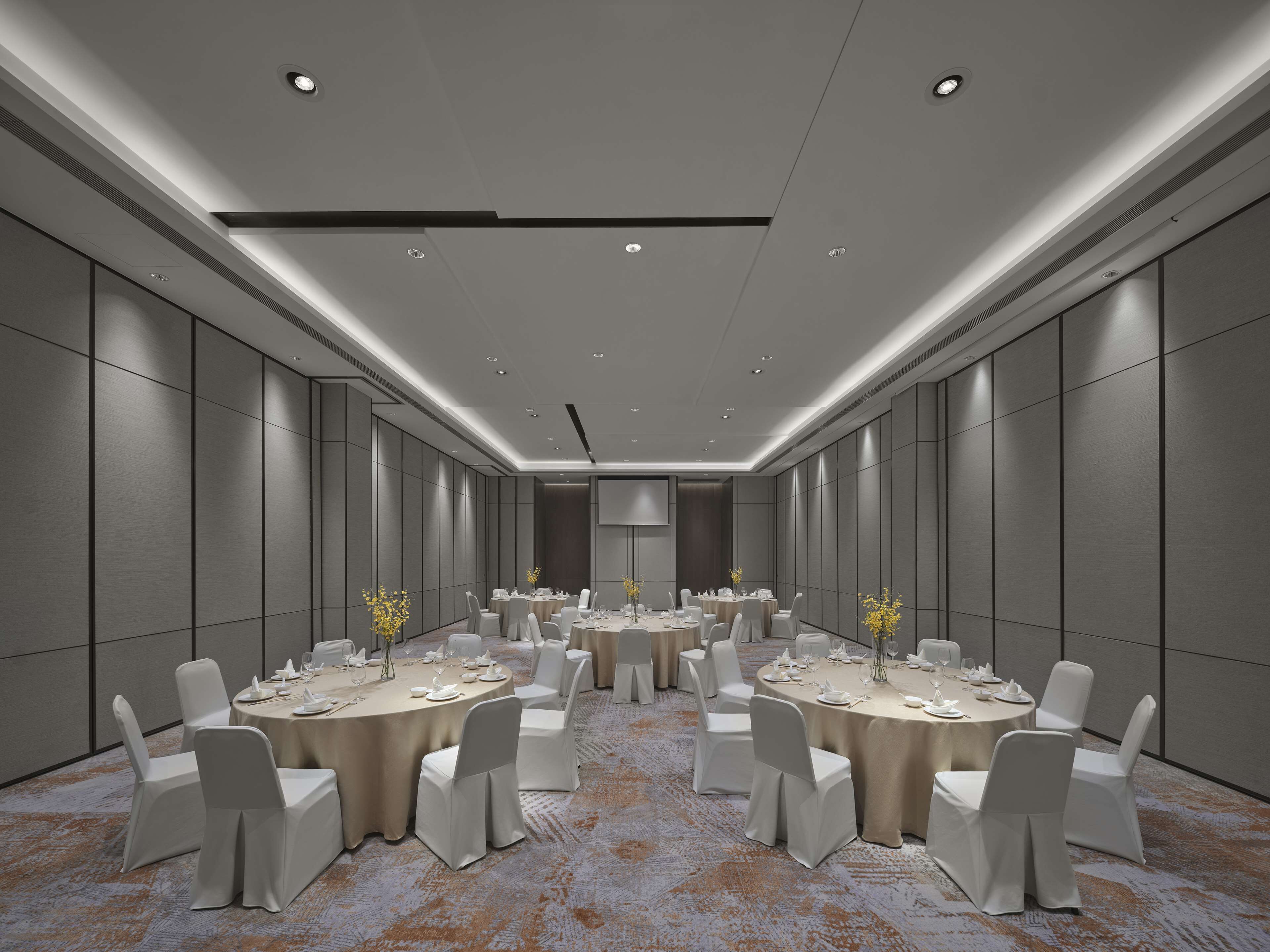 A conference room with round tables, white chairs, and a carpeted floor.