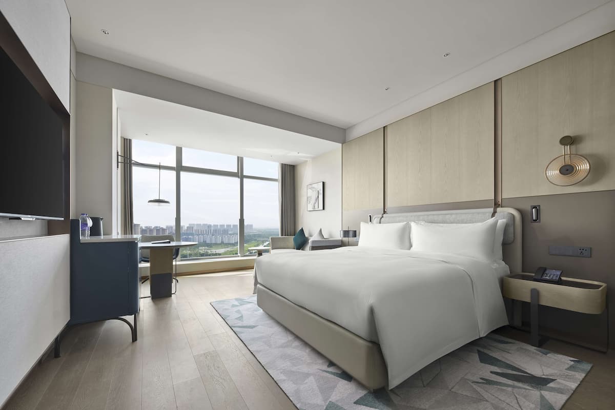 A modern hotel room with a large bed, a desk, and a view of the city.