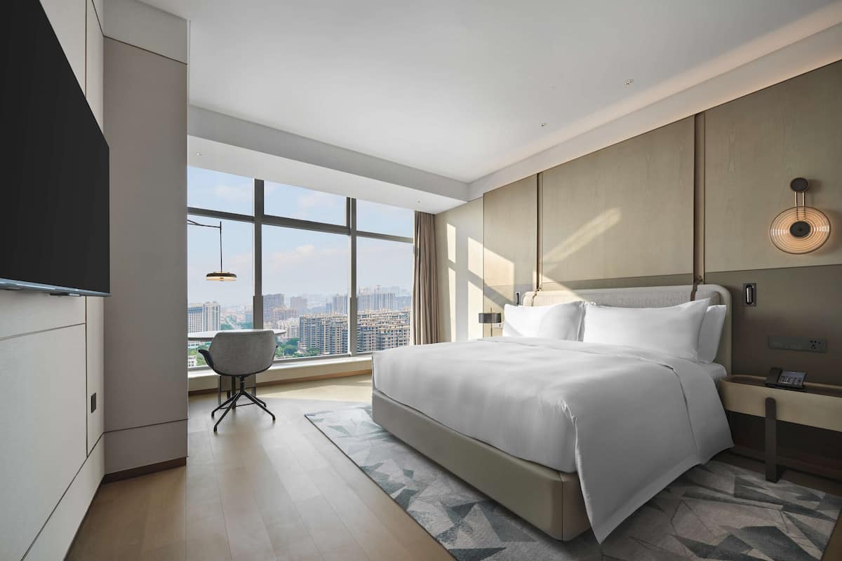 A modern hotel room with a large bed, a desk, and a city view through the window.
