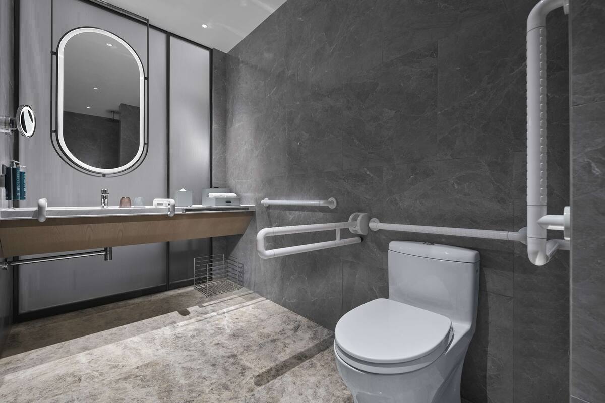 A modern bathroom with a marble floor, a white toilet, a large mirror, and a vanity with a towel rack.