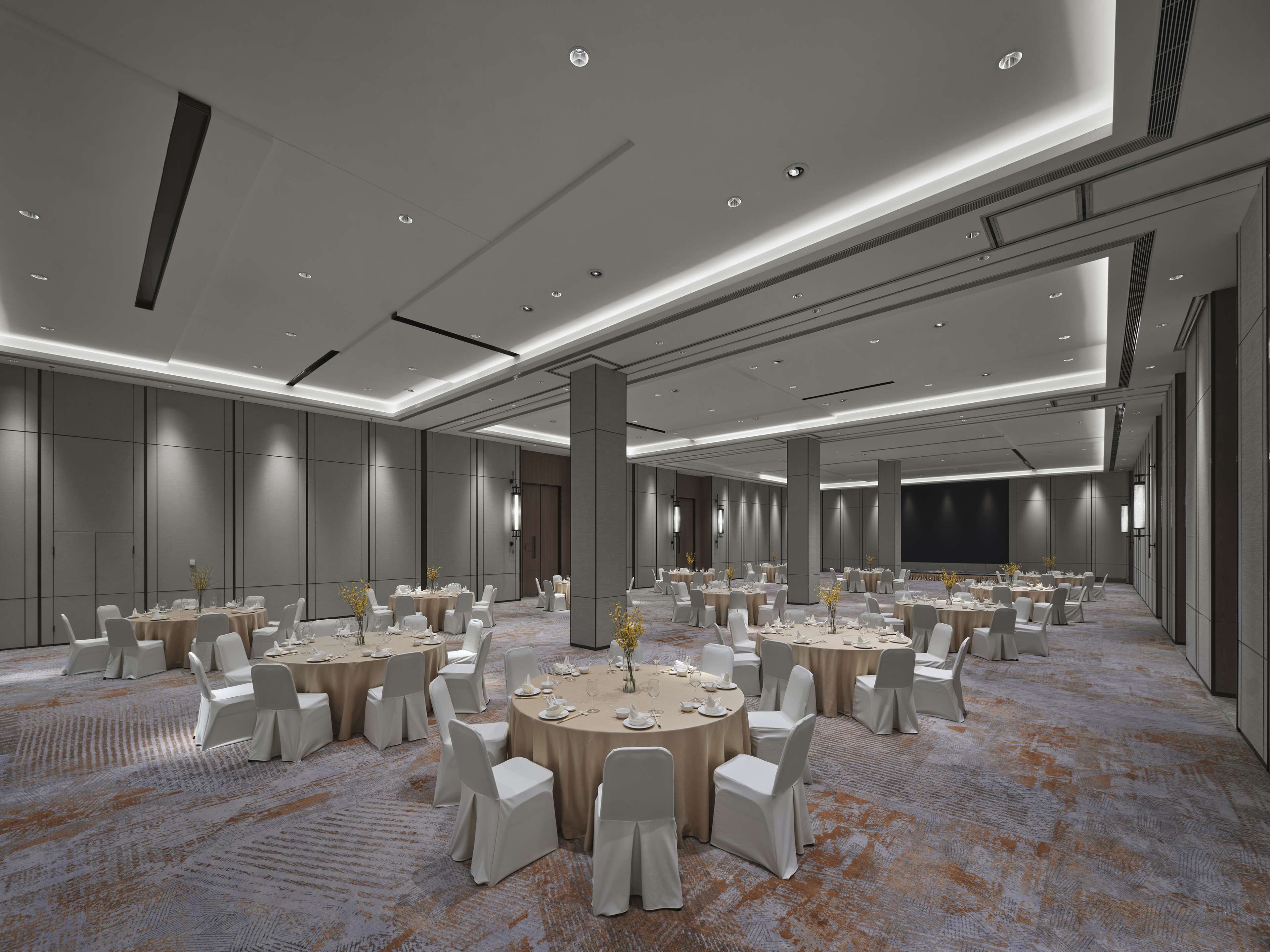 Un amplio salón de conferencias con varias mesas redondas, sillas blancas y piso alfombrado.