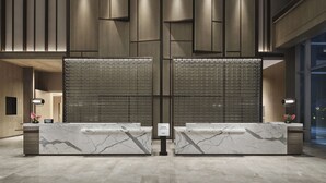 Zona de recepción de hotel con mostradores de mármol, diseño moderno y un amplio separador de vidrio.