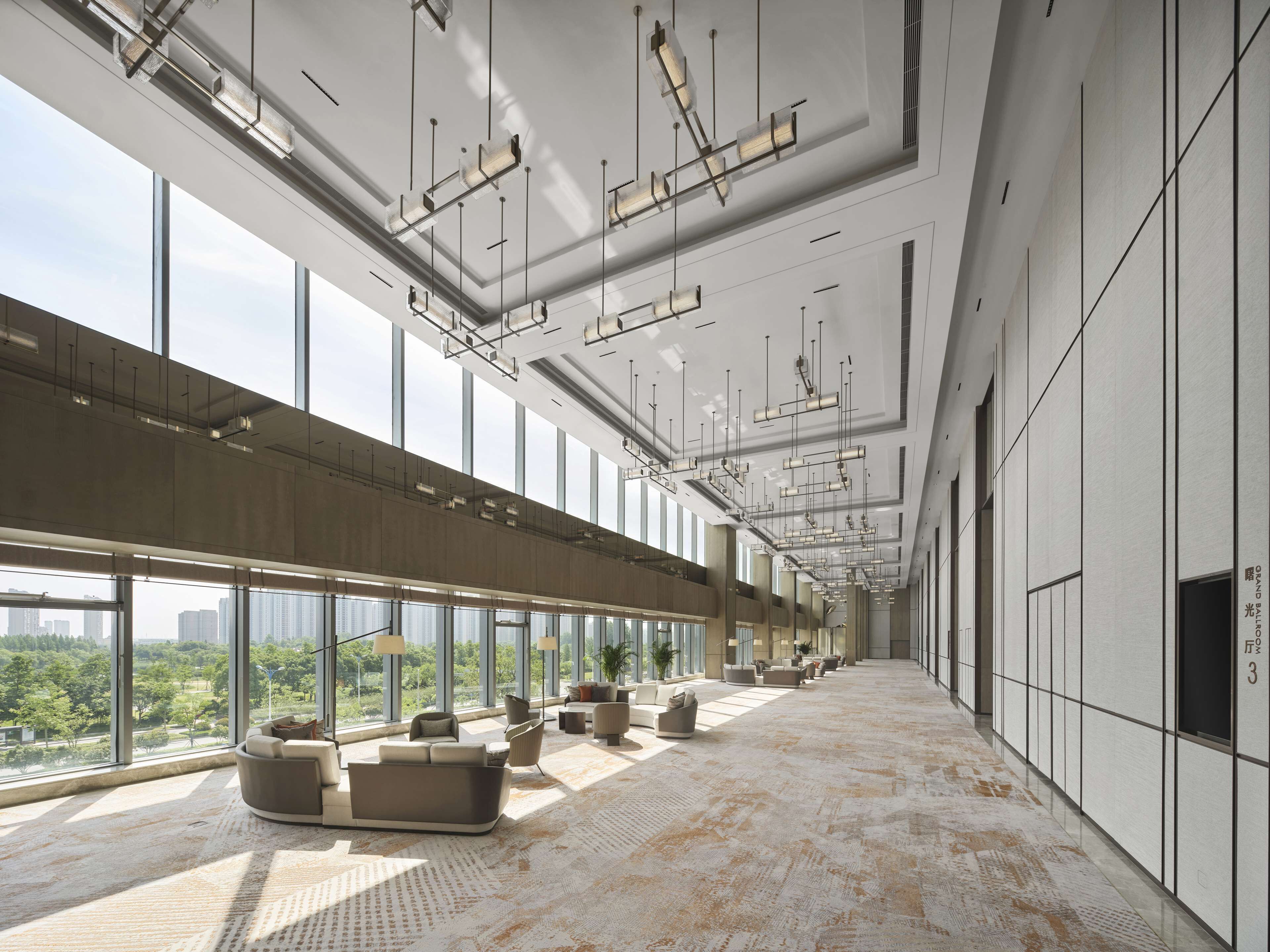 A spacious hotel lobby with large windows, modern lighting fixtures, and a high ceiling.