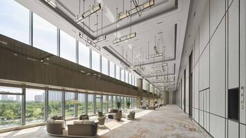 A spacious hotel lobby with large windows, modern lighting fixtures, and a high ceiling.