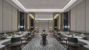 A modern hotel lobby with a symmetrical layout, featuring a central round table, seating arrangements, and a patterned carpet.