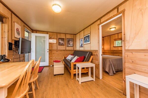 A cozy wooden cabin with a dining area, a sofa, and a bed.
