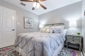 Ein Schlafzimmer mit einem Bett, zwei Nachttischlampen, einem Deckenventilator, einer Tür und einem Teppich mit floralem Muster.