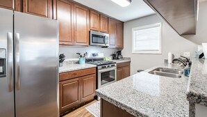 Una cocina moderna con electrodomésticos de acero inoxidable, armarios de madera y encimeras de granito, además de un microondas integrado.