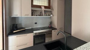 A compact kitchen with a stove, oven, sink, and a small countertop. - Angiolina apartment in Baveno with terrace (Baveno)