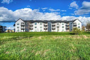 A multi-story residential building with balconies, a grassy lawn in front, and a clear sky. - King Bed Condo | Country Views | 5 Min From MSU (Bozeman)