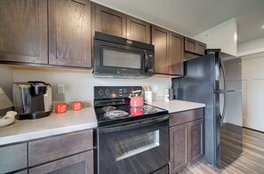 A modern kitchen with dark wooden cabinets, a stainless steel microwave, a black refrigerator, a red kettle, and a coffee maker. - King Bed Condo | Country Views | 5 Min From MSU (Bozeman)