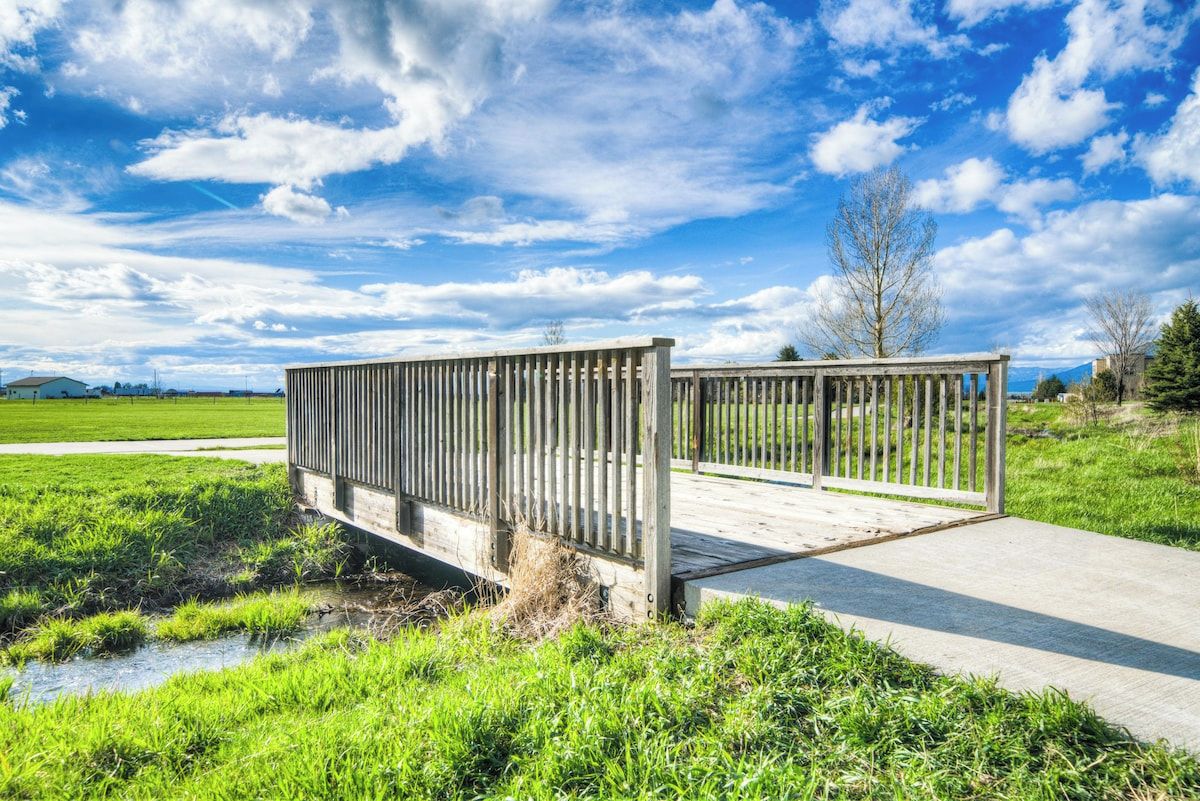 Eine Holzbrücke über einem Bach in einem grünen Feld, bewölkter Himmel.