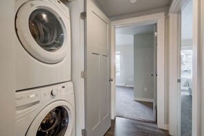 A laundry room with stacked washing machines and a door leading to a hallway. - King Bed Condo | Country Views | 5 Min From MSU (Bozeman)