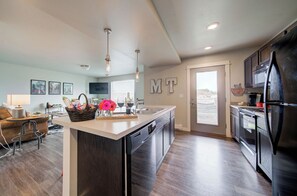 A modern kitchen with a central island, dark cabinetry, and a refrigerator. - King Bed Condo | Country Views | 5 Min From MSU (Bozeman)