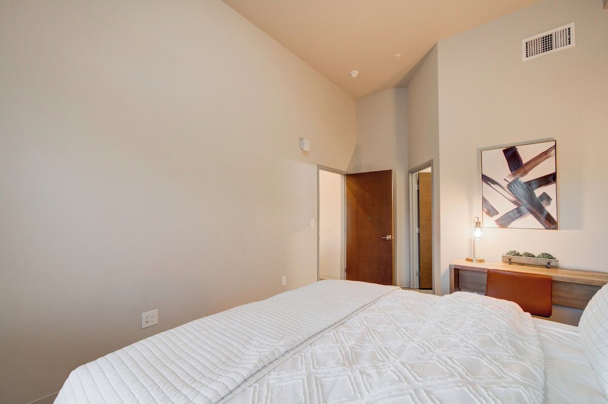 Une chambre à coucher comprenant un lit, une table de chevet, une commode, une lampe fixée au mur et une porte donnant sur une autre pièce.