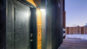 Un bâtiment moderne doté d’une grande porte d’entrée de couleur sombre et d’un petit luminaire placé juste au-dessus.