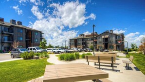 Un bâtiment moderne à plusieurs étages, doté d’un parking et d’un espace pique-nique avec des bancs.