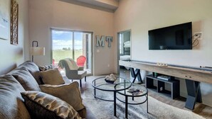 Una sala de estar moderna con un televisor grande, asientos cómodos y una mesa de centro de vidrio.