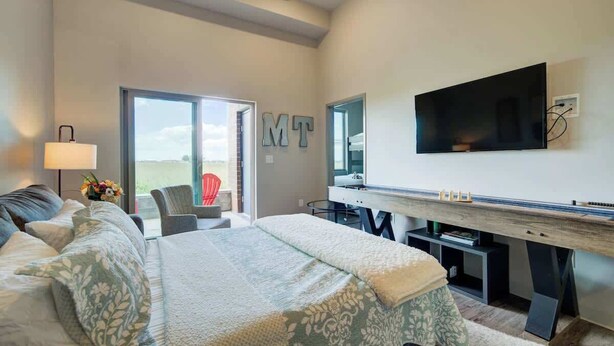 Un dormitorio moderno con una cama grande, un televisor montado en la pared y un ventanal corredero que da a un balcón.