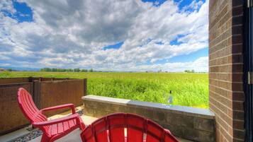 Un balcon avec des chaises rouges, une bordure en béton et une vue sur un champ verdoyant sous un ciel partiellement nuageux.
