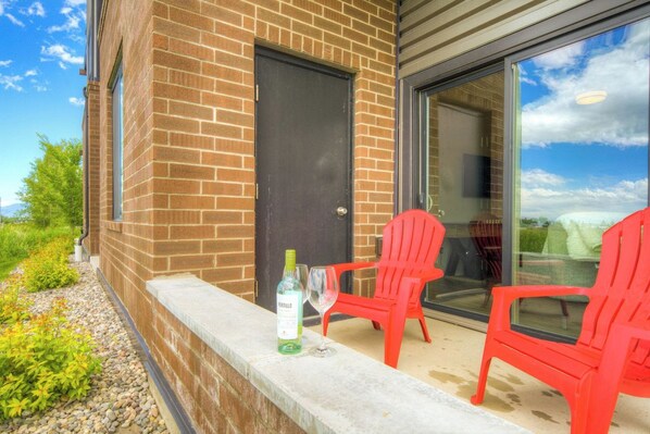 A brick building with a glass door and windows, a patio with red chairs, and a bottle of wine on the ledge. - Yellowstone Country | Mountain Views | Walk to MSU (Bozeman)