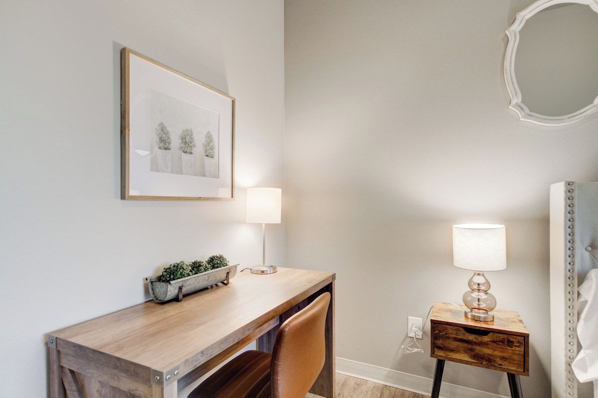 A hotel room with a wooden desk, two bedside lamps, a framed picture on the wall, and a mirror.