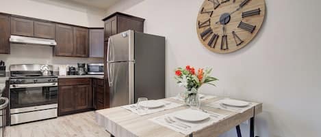 A modern kitchen with dark wood cabinets, stainless steel appliances, and a wooden dining table set for two with a vase of flowers.