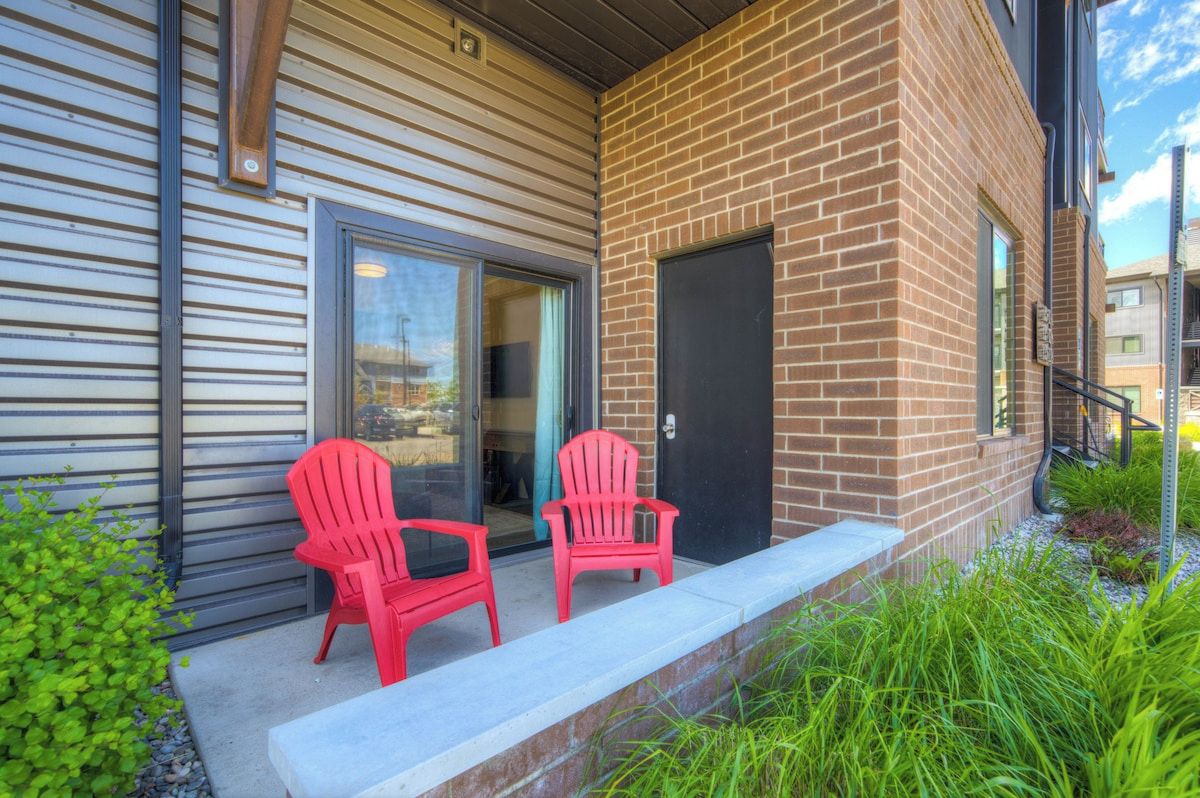 A building with a brick facade, a sliding glass door, and a small outdoor seating area with two chairs.
