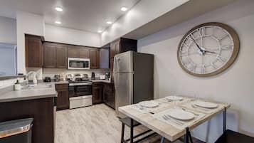 A modern kitchen with dark wooden cabinets, stainless steel appliances, a large wall clock, and a dining area set for four.