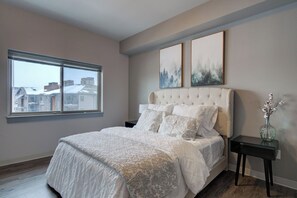 A bedroom with a large bed, a nightstand, a vase with flowers, and two framed pictures on the wall.