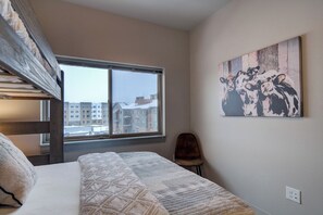 A bedroom with a bunk bed, a large window, a chair, and a wall-mounted artwork.