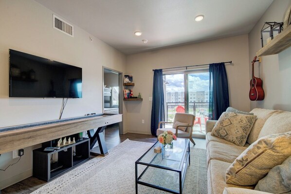 A living room with a flat-screen TV, a coffee table with a vase, a sofa, and a guitar on the wall.