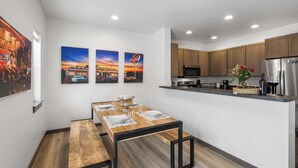 A modern kitchen with wooden cabinets, a stainless steel refrigerator, and a dining area with a wooden table and benches. - Downtown Duplex | Game Room | Mountain Music (Bozeman)