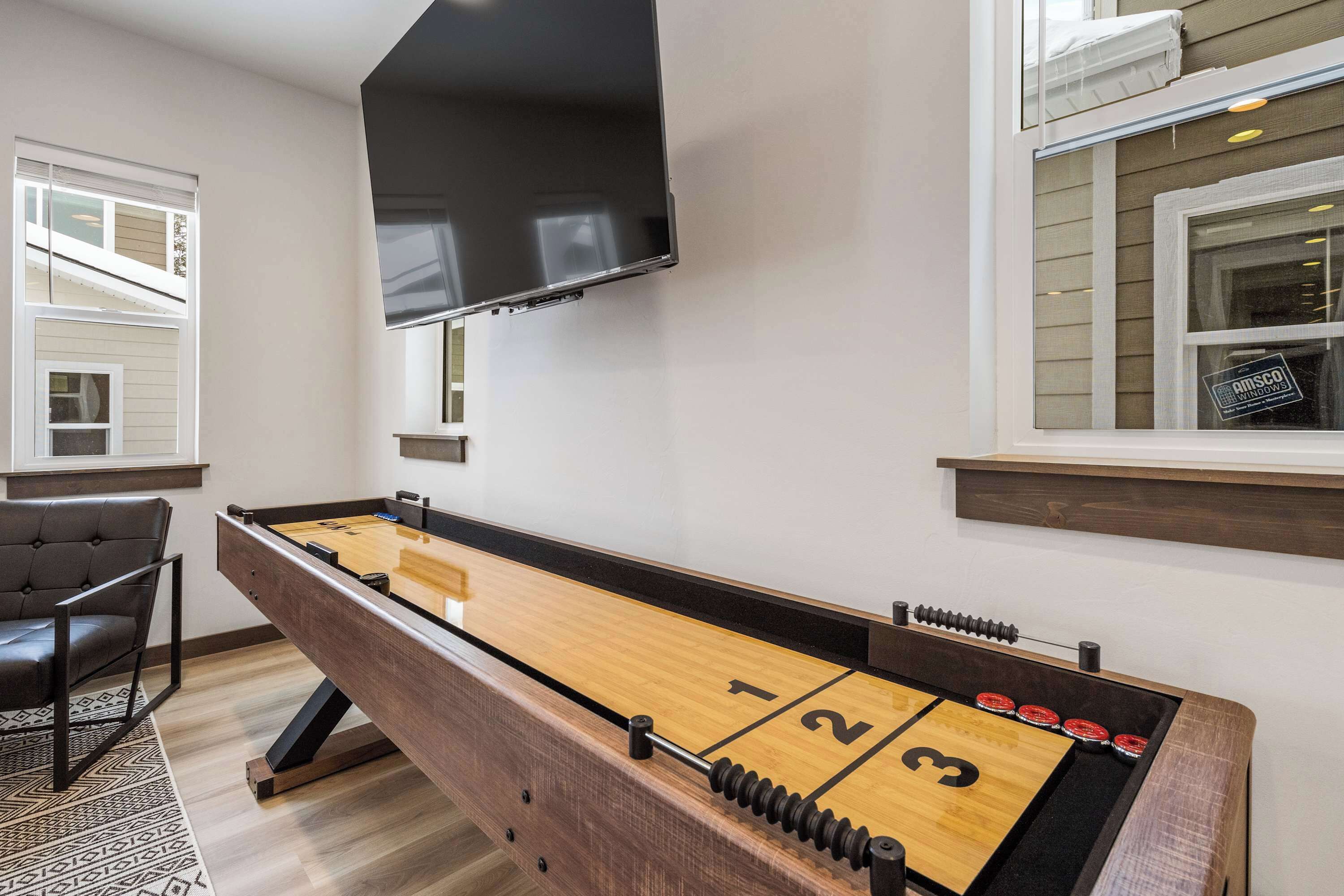 A foosball table in a room with a TV mounted on the wall and a window with blinds.