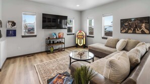 A modern living room with a sofa, a coffee table, and a flat-screen TV mounted on the wall. - Downtown Duplex | Game Room | Mountain Music (Bozeman)