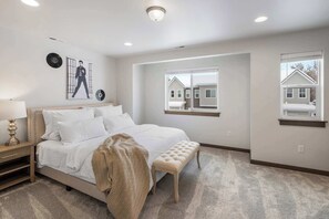 A bedroom with a bed, bedside table, lamp, and a window with a view of neighboring houses. - Heart of Bozeman | Juke Box Jet Away (Bozeman)