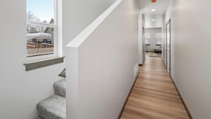 Un pasillo estrecho con suelo de madera, una ventana que da a una casa y una escalera.
