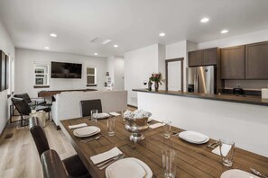 Una cocina moderna con armarios oscuros, un refrigerador de acero inoxidable y un comedor con una mesa de madera dispuesta para cuatro comensales.