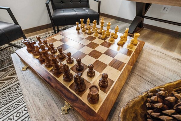 Un tablero de ajedrez con las piezas colocadas en una sala de estar con una alfombra estampada, un sofá de cuero negro y una mesa de centro de madera.