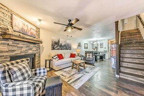 A spacious living room with a stone fireplace, a ceiling fan, and a staircase leading to another level. - Cozy Ruidoso Condo w/ Grill & Mountain Views! (Ruidoso)